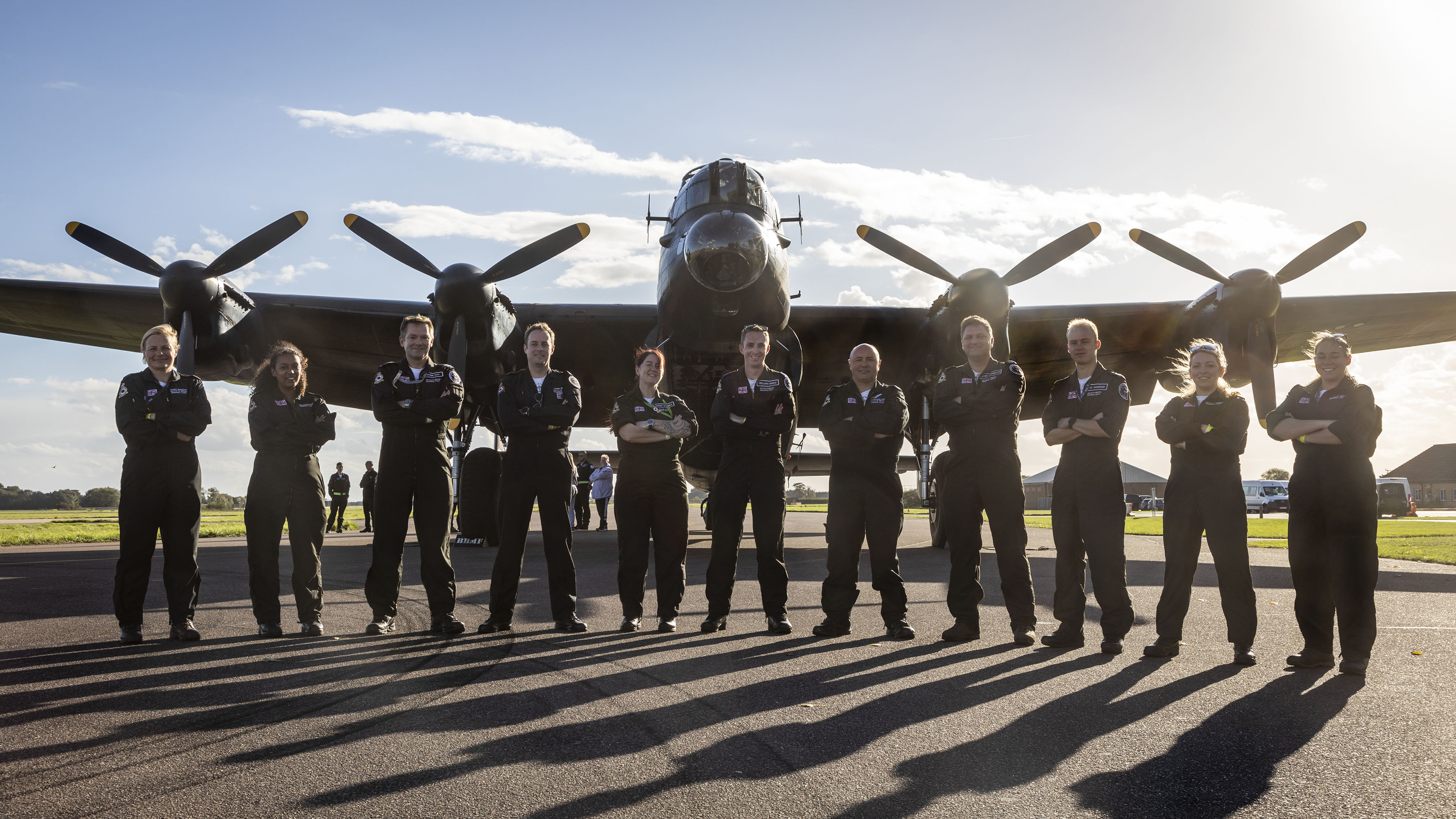 Image shows the Battle of Britain Memorial Flight team standing in front of their Lancaster Bomber aircraft.